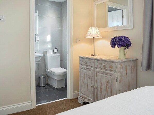 A bathroom with a toilet, sink, and mirror. There is a cabinet with drawers and a vase with flowers.