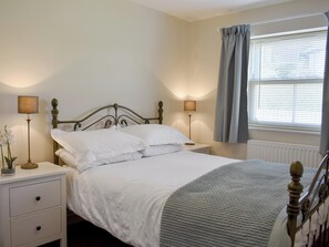A neatly made bed with white linens, a bedside table with a lamp, and a window with curtains. - 3 bedroom accommodation in Leyburn (Leyburn)