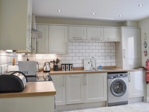 A modern kitchen with white cabinets, a stainless steel kettle, a washing machine, and a sink with a faucet.