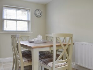 A dining area with a table, chairs, a clock, and a window with blinds. - 3 bedroom accommodation in Leyburn (Leyburn)