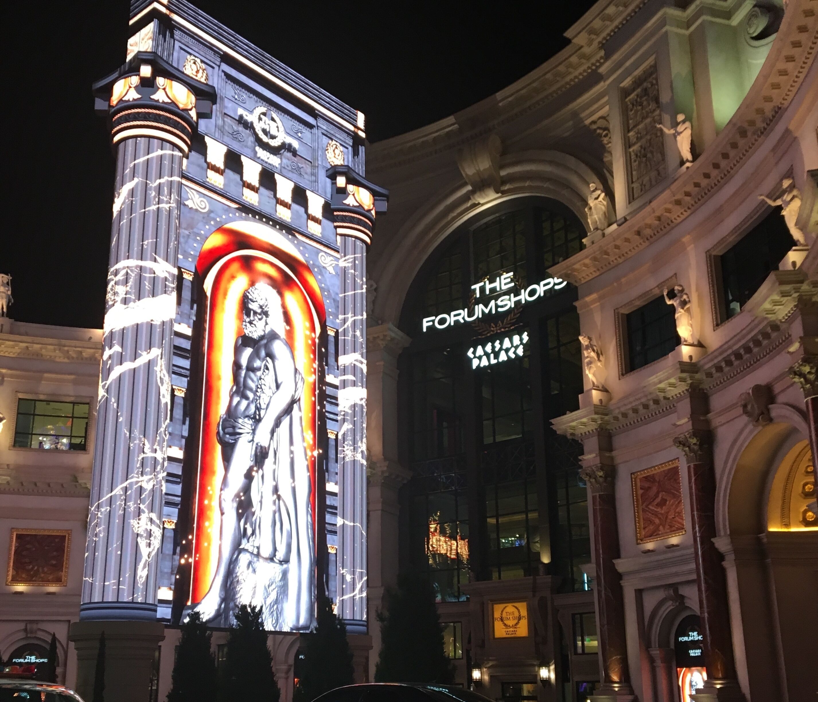 A building with a large illuminated statue and a sign reading "The Forum Shops at Caesars Palace".