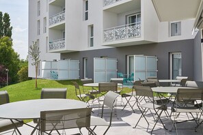 Un edificio moderno con balcones, mobiliario exterior y un césped bien cuidado.