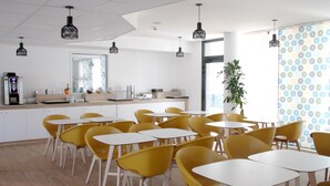 Moderni ruokailutila, jossa on keltaiset tuolit ja valkoiset pöydät, kahvinkeitin ja suuri ikkuna, josta on kaunis näköala.