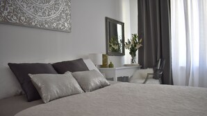 A neatly made bed with a white and grey duvet, a small bedside table with a lamp and a vase, and a mirror on the wall. - Split Centre VIVERE Apartment (Split)