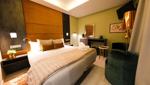 A modern hotel room with a large bed, a green armchair, a small table, and a TV mounted on the wall. - Hercules Boutique Hotel (Ceuta)