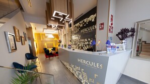 A reception desk at Hercules Boutique Hotel with a modern design, framed pictures on the wall, and a staircase in the background. - Hercules Boutique Hotel (Ceuta)