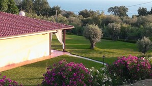 Una casa con techo de tejas rojas, un jardín con flores rosadas y vista al mar.