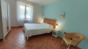 Un dormitorio con cama, mesita de noche, silla y ventana con cortinas.