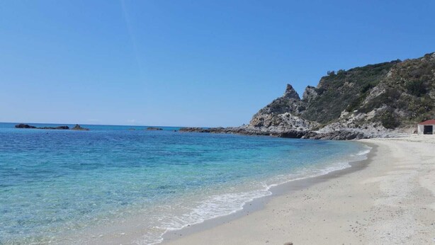 Una playa con aguas turquesas cristalinas, una orilla arenosa y acantilados rocosos.