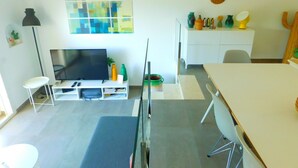 A modern living room with a flat-screen TV, a dining table, and a kitchen area with a white cabinet and decorative items. - Modern house overlooking the sea, near the beach in Almadraba, Roses (ROSES)