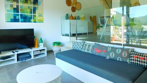 A modern living room with a large flat-screen TV, a sofa with patterned cushions, a coffee table, and a staircase leading to an upper level. - Modern house overlooking the sea, near the beach in Almadraba, Roses (ROSES)