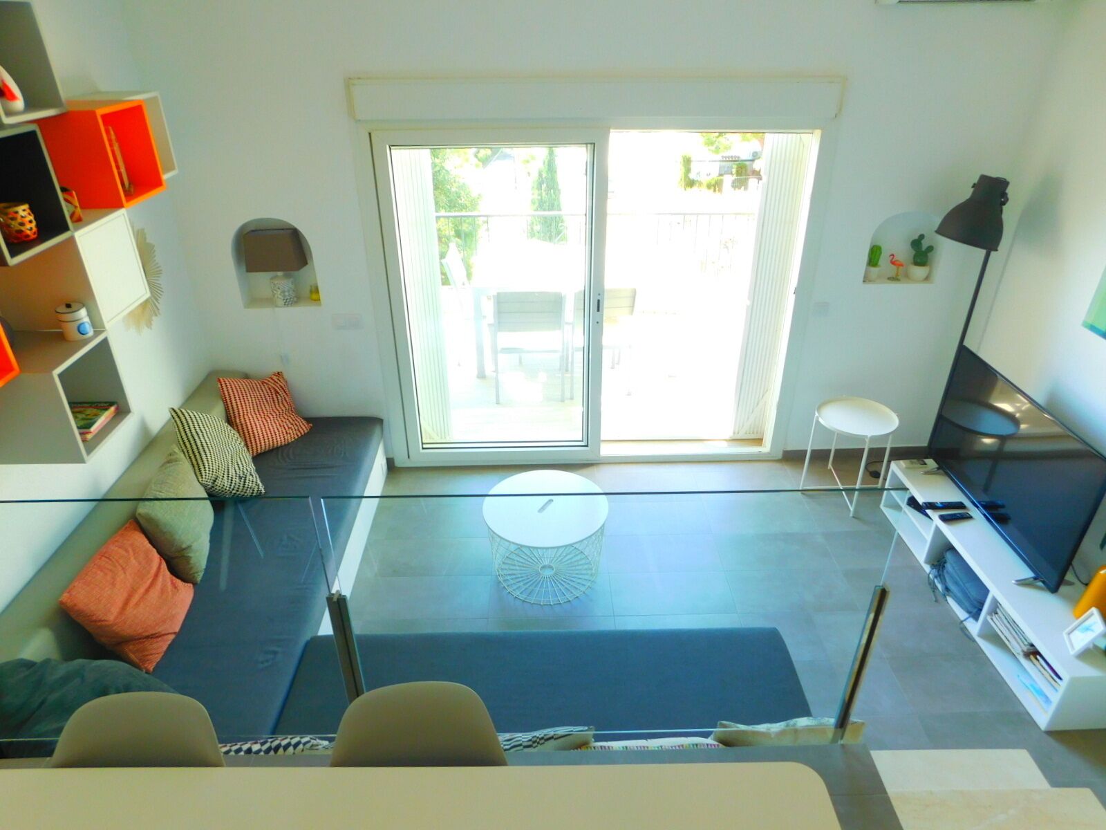 A modern living room with a glass wall, a sofa, a TV, and a dining area.