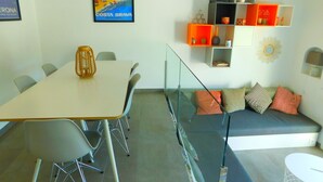 A modern living room with a glass partition, a dining area with a table and chairs, and a colorful wall decoration. - Modern house overlooking the sea, near the beach in Almadraba, Roses (ROSES)