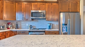 A modern kitchen with wooden cabinets, stainless steel appliances, and a marble countertop.