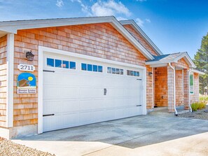 A two-story house with a white garage door, a wooden exterior, and a clear blue sky.
