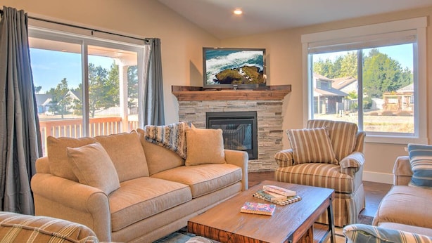 A living room with a sofa, armchairs, a coffee table, a fireplace, and large windows with a view of the outside.