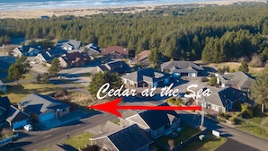 An aerial view of Cedar at the Sea, featuring a residential area with houses, a road, and a view of the ocean and beach.