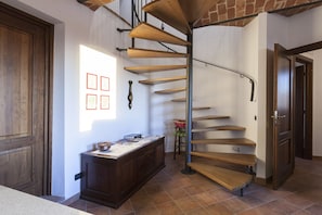 Una escalera de caracol con escalones de madera y barandillas de metal, que conduce a un rellano con un escritorio de madera y un ventanal.