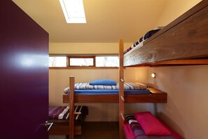 Une chambre avec un lit superposé, une lucarne, une fenêtre et une table de chevet.