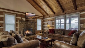 L’intérieur d’un chalet confortable, avec des murs en rondins de bois, une cheminée en pierre, des canapés en cuir et un téléviseur fixé au mur.
