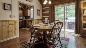 Een eethoek met een houten tafel voor vier personen, omringd door houten stoelen. Achtergrond is een keuken zichtbaar, en er is een glazen schuifdeur die leidt naar een buitenruimte met een barbecue.