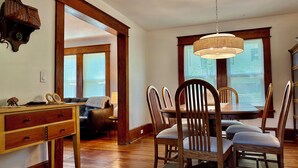 Ein Essbereich mit Holzsesseln und einem Tisch, ein Schreibtisch aus Holz mit Schubladen, eine Lampe und eine Pendelleuchte.