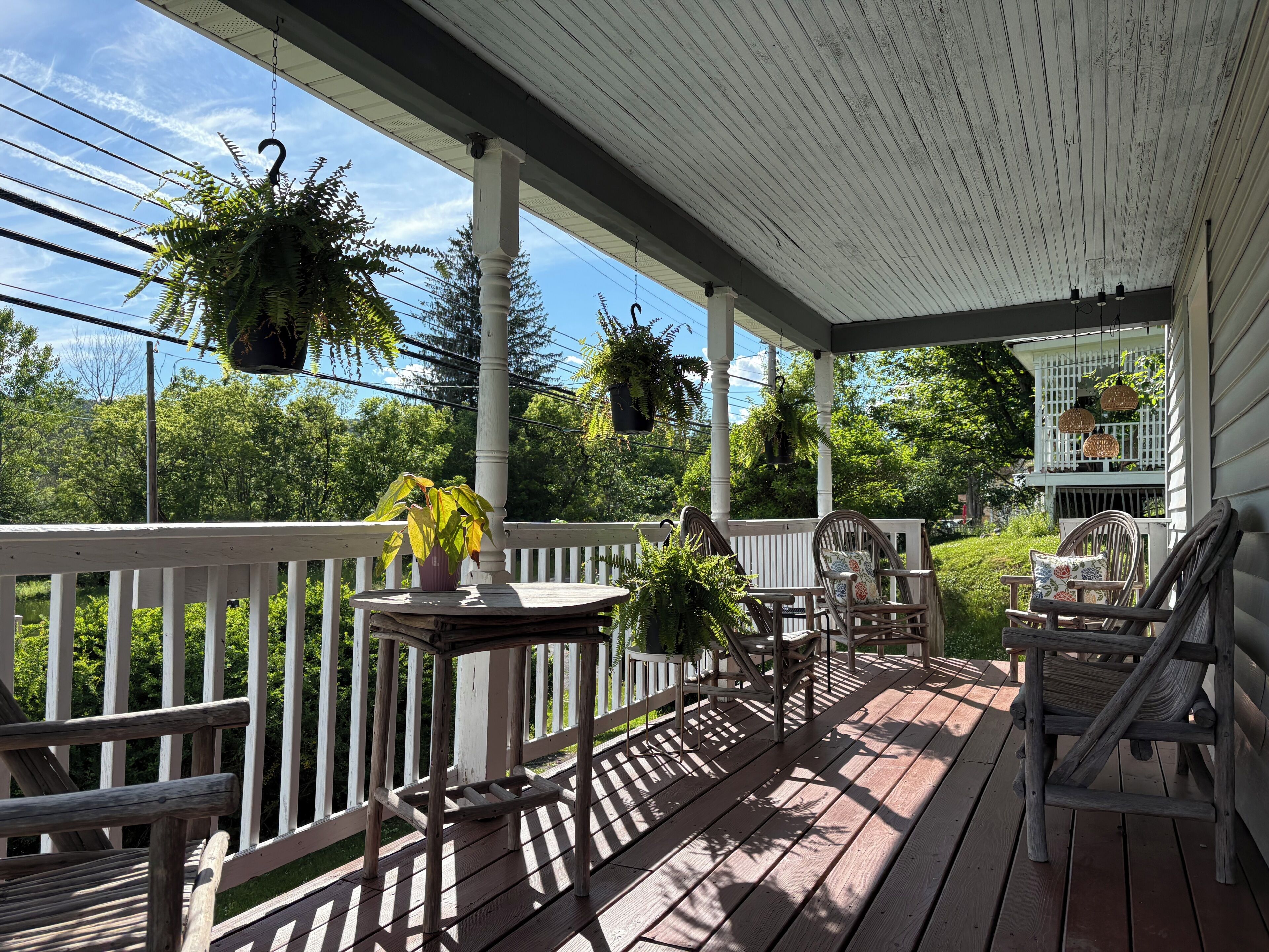 Une terrasse en bois avec une rambarde blanche, des jardinières suspendues et du mobilier d’extérieur.