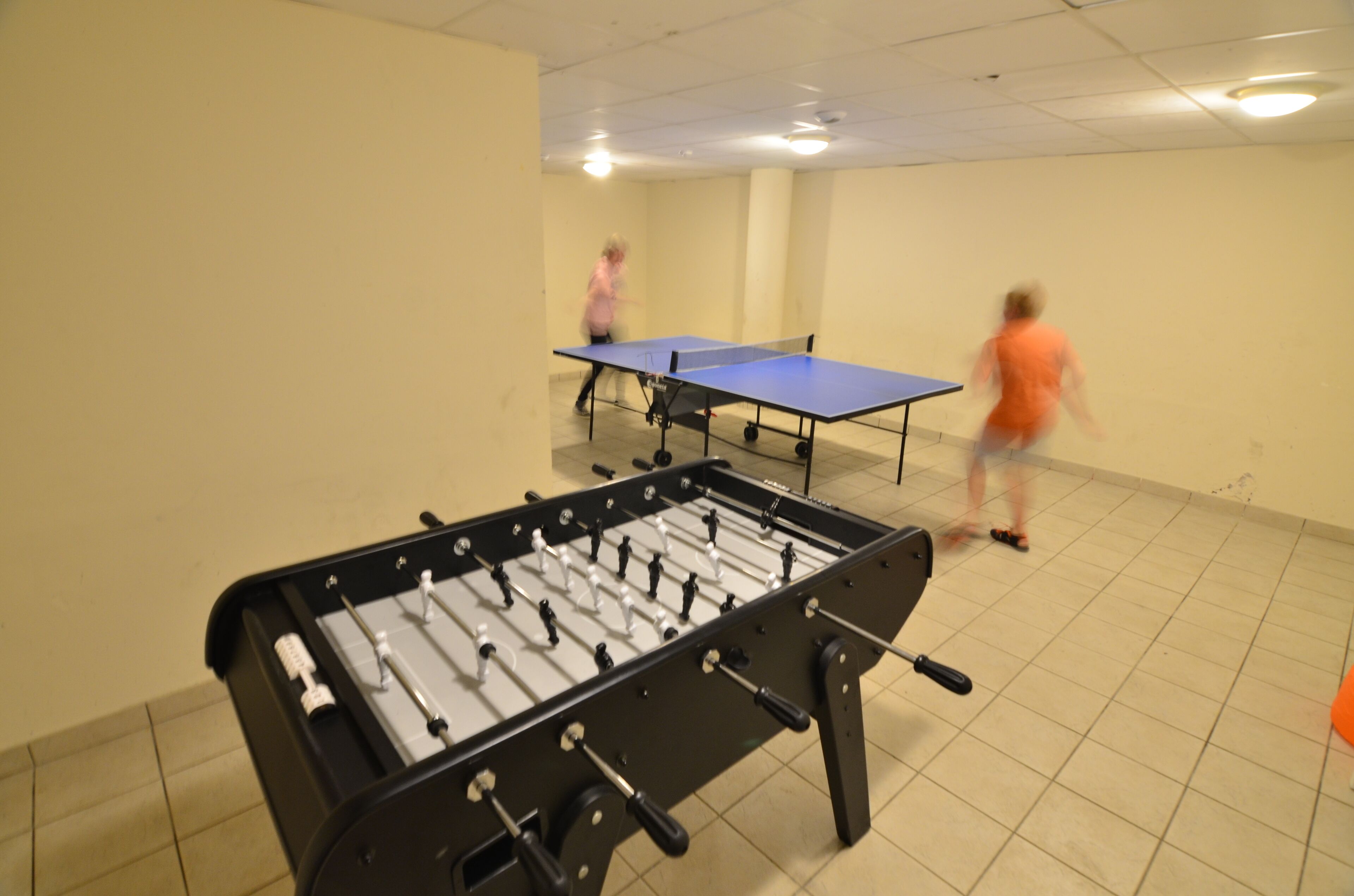 A room with two foosball tables and a ping pong table.