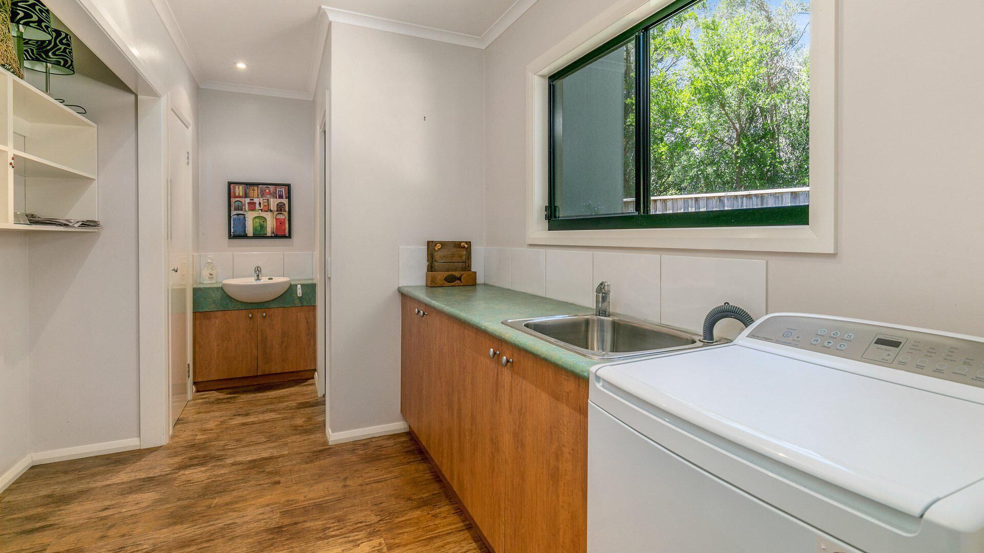 A compact kitchen with a built-in washer and dryer, a sink, and a window overlooking greenery.