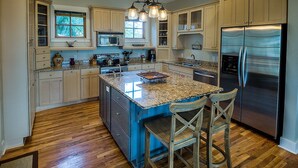 Una cocina con armarios de madera, un refrigerador de acero inoxidable, una encimera de granito y un taburete de bar.