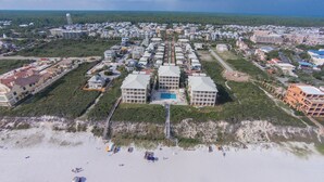Vista aérea de un complejo turístico costero con varias edificaciones, una piscina central y una zona de playa.