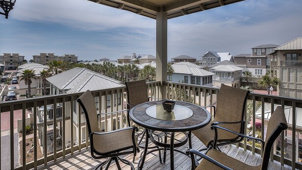 Un espacio al aire libre cubierto con una mesa redonda y cuatro sillas, con vista a un barrio residencial con casas y palmeras.