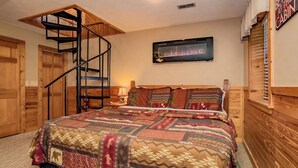 A bedroom with a large bed, a wooden headboard, a built-in TV, a fireplace, and a spiral staircase. - Rocking Bear: Mtn View! Pets, S/Secluded, Hot Tub, Wifi, Games, Spacious Decks! (Sevierville)