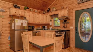 A wooden cabin kitchen with a dining table, chairs, a refrigerator, stove, microwave, and cabinets. - Rocking Bear: Mtn View! Pets, S/Secluded, Hot Tub, Wifi, Games, Spacious Decks! (Sevierville)