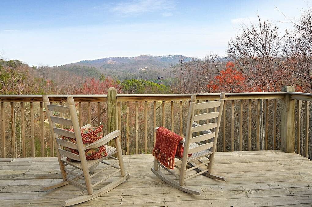 Eine Holzterrasse mit zwei Schaukelstühlen und Blick auf einen bewaldeten Hang.