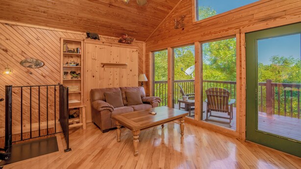 A wooden interior with a sofa, coffee table, and a view of the outdoors through large windows. - Rocking Bear: Mtn View! Pets, S/Secluded, Hot Tub, Wifi, Games, Spacious Decks! (Sevierville)