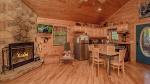 A cozy cabin-style kitchen with a stone fireplace, wooden cabinets, and a dining area. - Rocking Bear: Mtn View! Pets, S/Secluded, Hot Tub, Wifi, Games, Spacious Decks! (Sevierville)