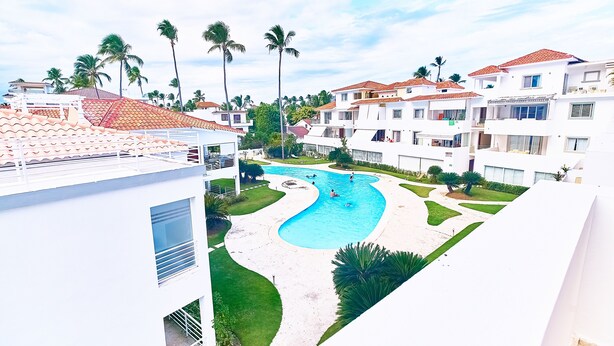 Zona residencial con piscina rodeada de palmeras y edificios blancos con techos de tejas rojas.