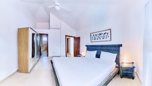 Un dormitorio con cama, mesita de noche, ventilador de techo, un cuadro en la pared y una puerta de madera.