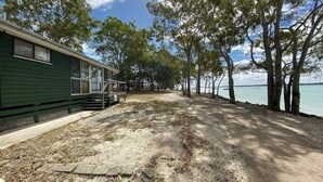 A green building with a porch and steps, a dirt path, and trees lining a body of water. - Stafford Hall - Burrum Heads- Riverfront- 3BR- Great Views (BURRUM HEADS)