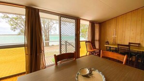 A room with a large window overlooking a beach, a wooden table, and a chair. - Stafford Hall - Burrum Heads- Riverfront- 3BR- Great Views (BURRUM HEADS)
