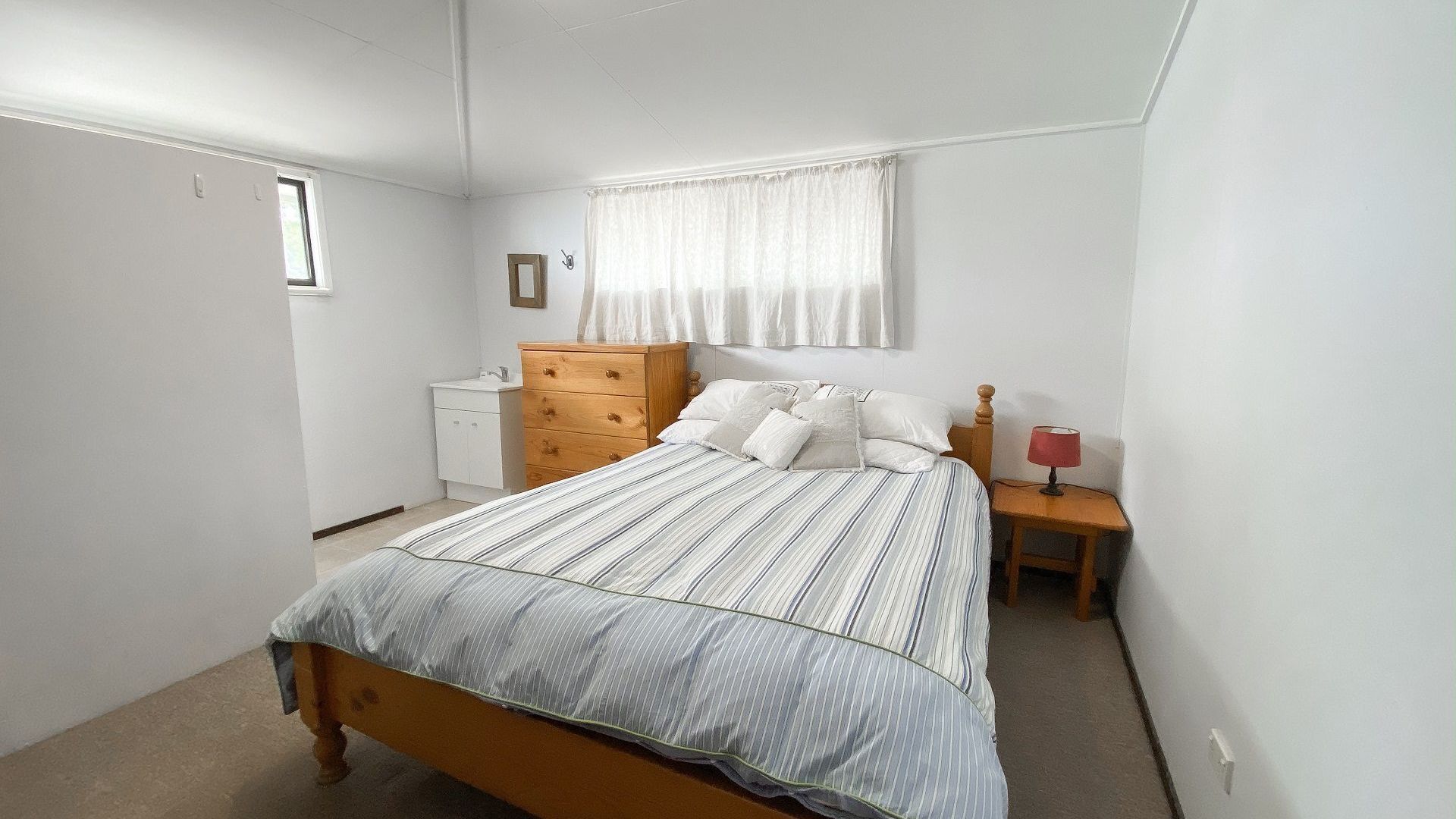 Une chambre à coucher comprenant un lit, une commode, une table de chevet, une lampe et une fenêtre avec des rideaux.