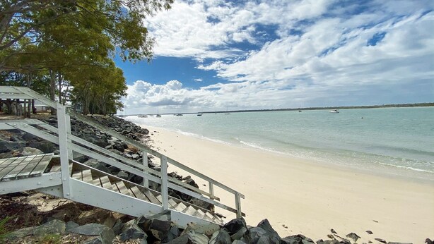 A beach with a staircase leading down to the shore, surrounded by rocks and trees. - Stafford Hall - Burrum Heads- Riverfront- 3BR- Great Views (BURRUM HEADS)