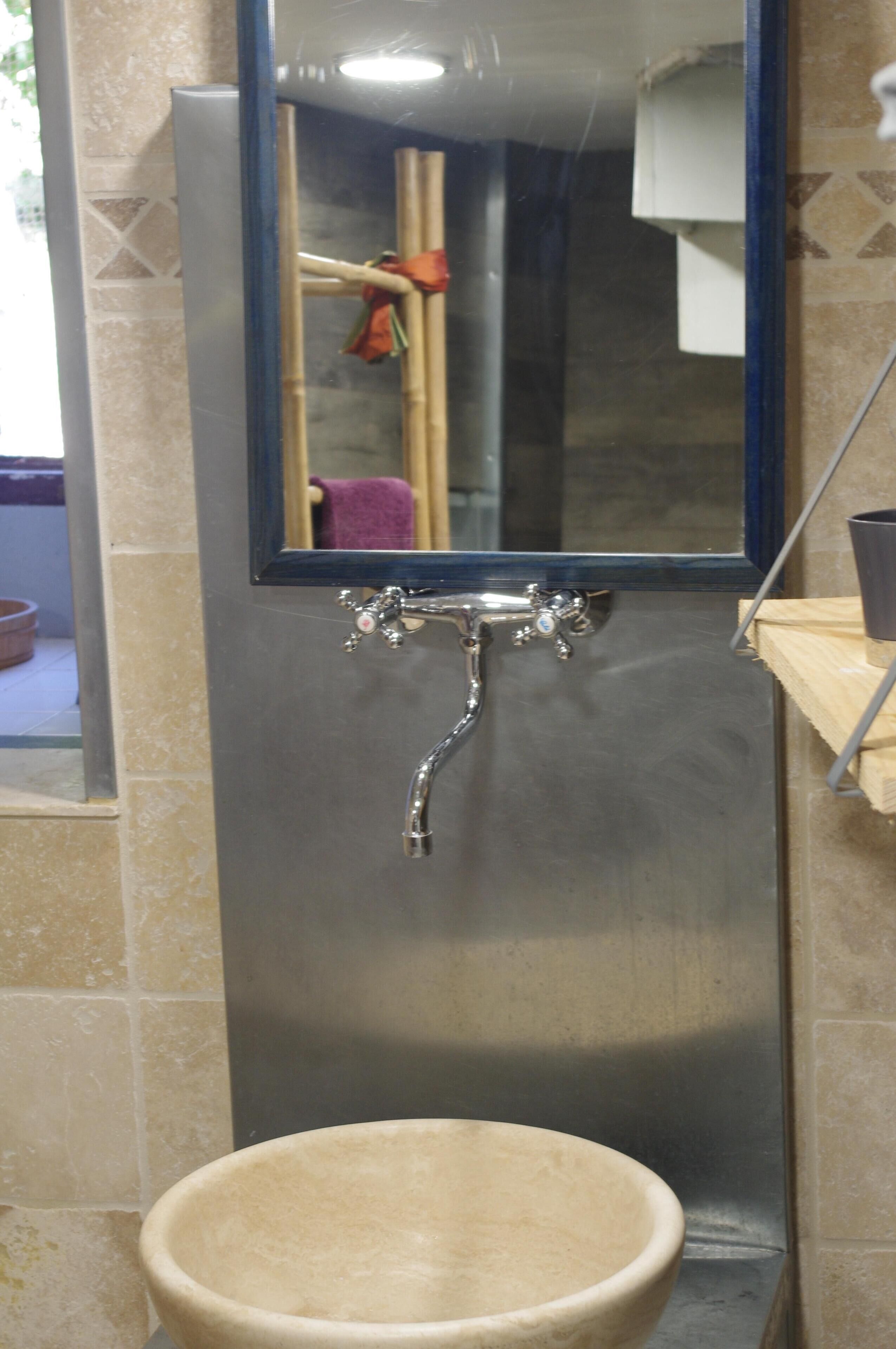 A bathroom with a stainless steel sink, a mirror, and a towel rack.