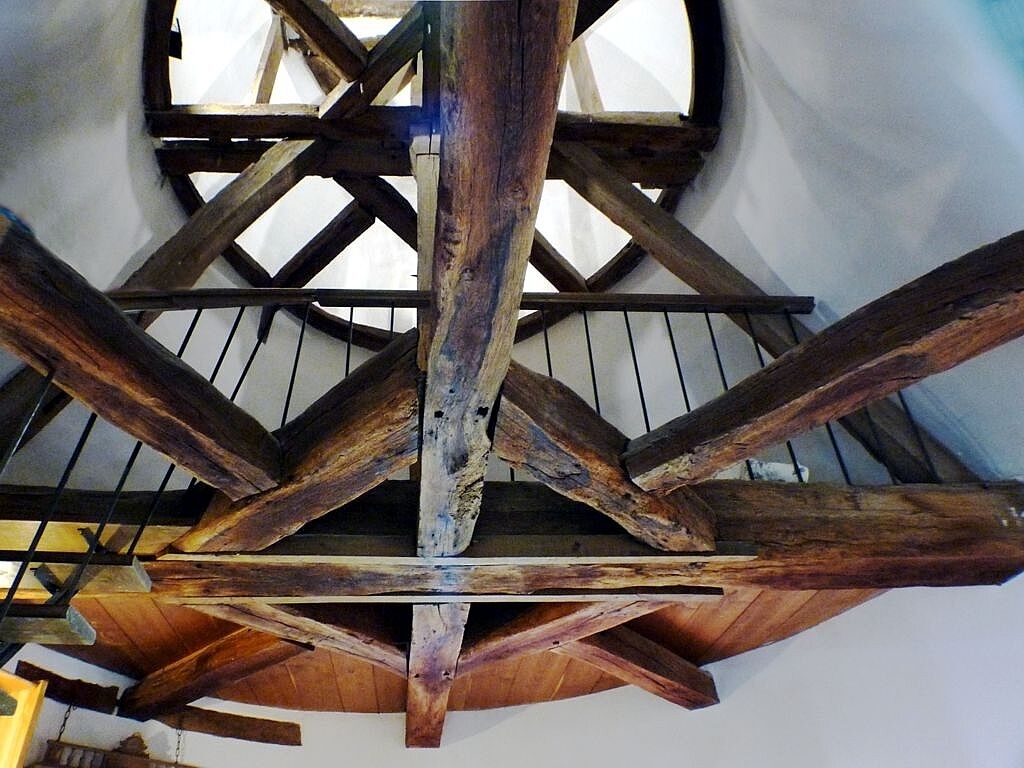 Estructura de techo de madera con vigas y un ventanal circular.