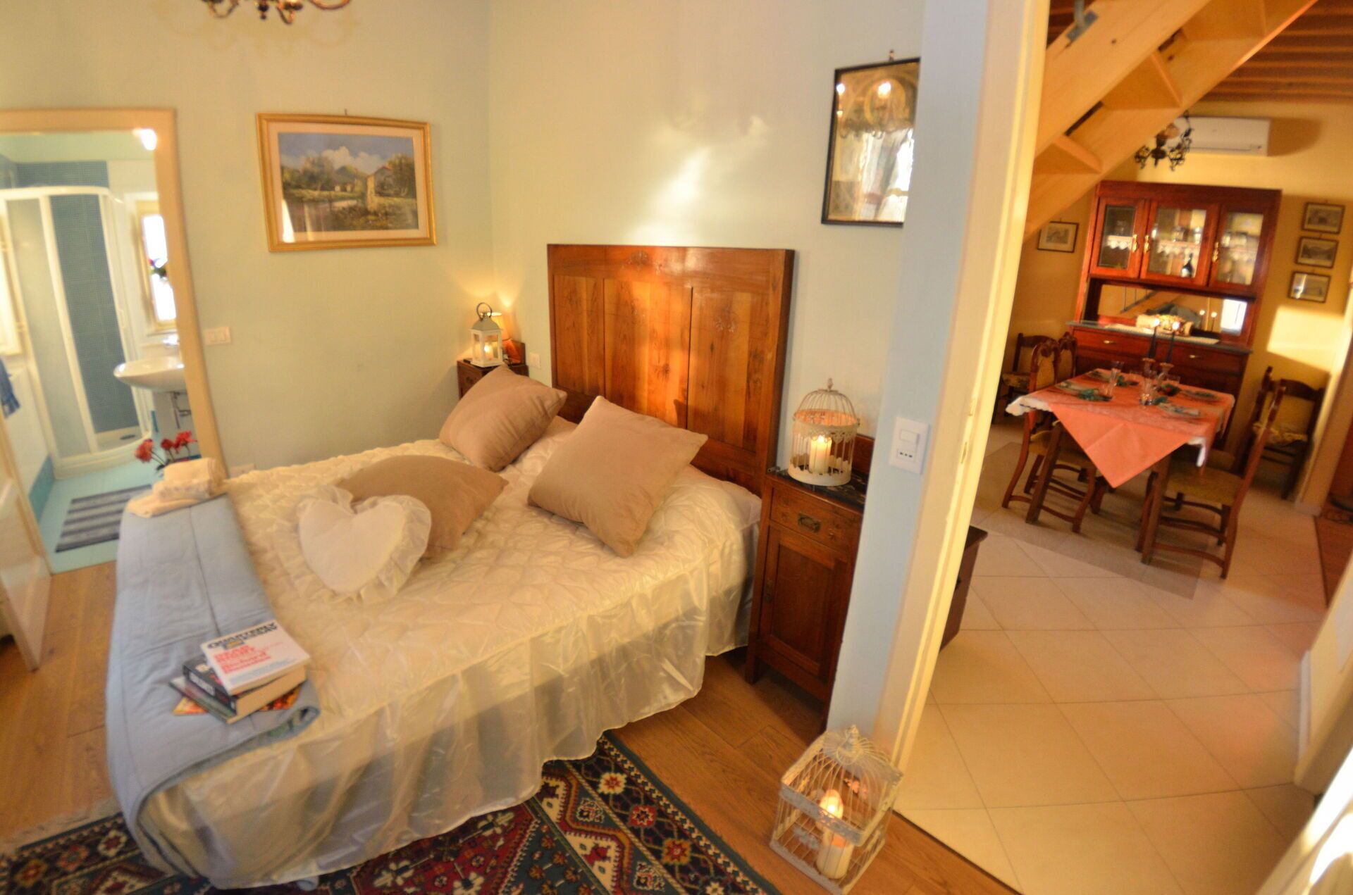 Un dormitorio con cabecera de madera, cama con sábanas blancas, mesita de noche con un farolillo y una zona de comedor con una mesa dispuesta para dos.