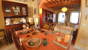 A dining area with a table set for four, featuring a wooden cabinet with glass doors, a chandelier, and a view of a person in the background. - Beautiful apartment for 7 people with A/C, WIFI, TV and panoramic view (Lucca)