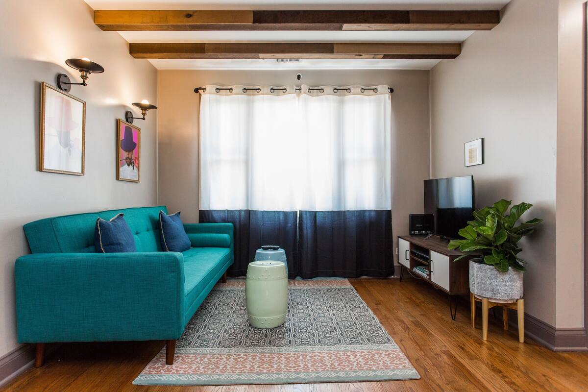 A living room with a teal sofa, a coffee table, a TV on a stand, and a potted plant.