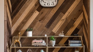 Huoneessa on puinen kalanruotokuvioinen katto, seinäkello sekä hyllyjä, joilla on erilaisia koriste-esineitä ja kirjoja.