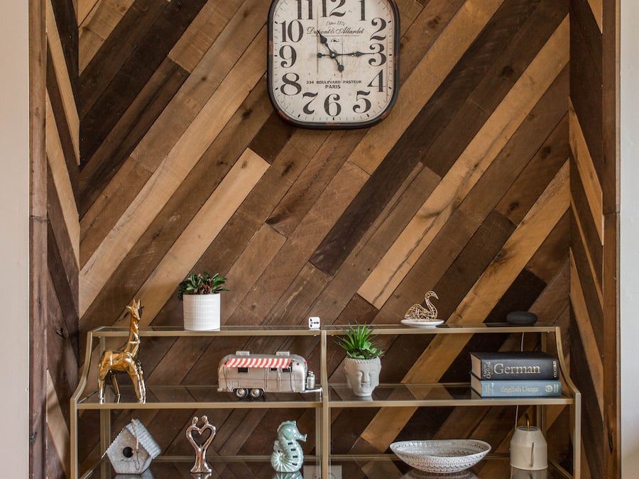 Une pièce avec un plafond en bois à motifs en chevrons, une horloge murale et des étagères ornées de divers objets décoratifs et de livres.